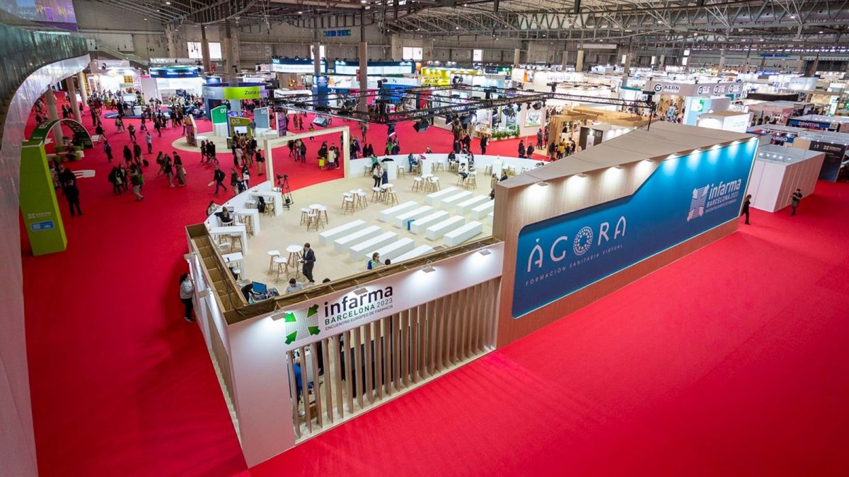 Stand de Infarma 2023 en una feria, con un diseño moderno y el logo de Infarma visible. El espacio está lleno de mesas y visitantes interactuando, mientras que se muestra un área de formación y un fondo vibrante con el logo del evento